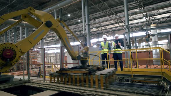 Working Engineers Check Robotic Arms, Moving Bricks.