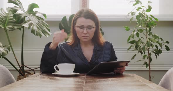 Breakfast Mature Woman in Pajamas with Cup of Tea Reading Digital Tablet, Bad News