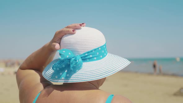 Happy Senior Woman in Sun Hat on Summer Beach. Age, Leisure and People Concept. Back View.