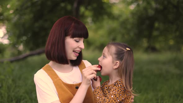 Video Portrait of Single Mom with Little Daughter is Engaged in Eating Strawberry Resting Outdoor