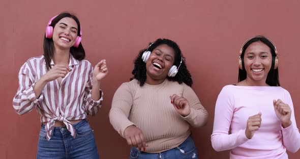 Happy latin girls having fun while dancing and listening music playlist with headphones