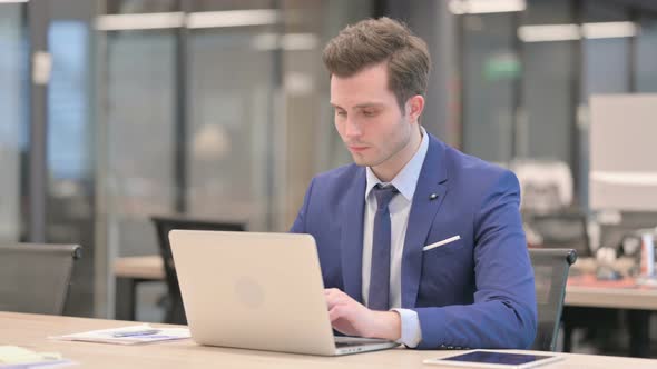 Businessman Looking at Camera While Using Laptop in Office