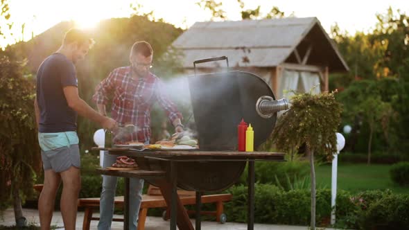 Two Caucasian Males Making Hamburgers with Fried Meat and Buns Near Barbecue Grill in Slowmotion