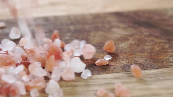 Himalayan rock salt on a rustic wooden surface. Falling orange pink crystals in slow motion. Macro