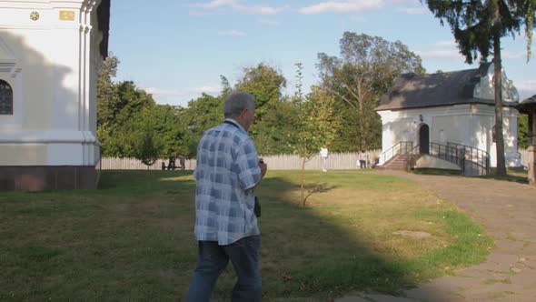 Retired Man with Camera on Neck Enjoys Walking Along Street