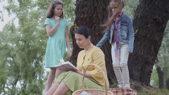 Elegant Senior Woman Sitting on the Blanket Under the Tree in the Park Reading the Book