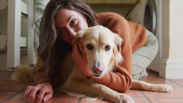 Smiling caucasian woman kissing and cuddling her pet dog sitting on floor at home