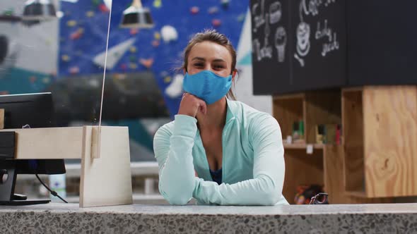 Caucasian woman wearing face mask leaning on counter at reception of indoor climbing gym