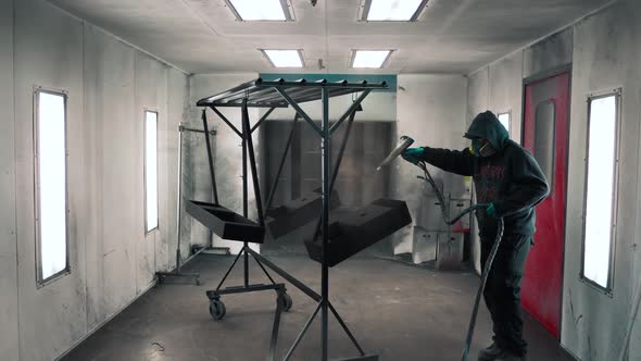 Man applying black anti-corrosion powder coating to metal sheet using a spray gun in factory.