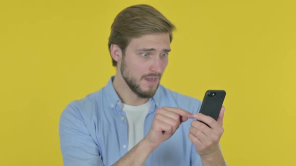 Young Man Loss on Smartphone on Yellow Background