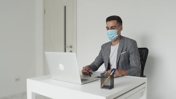 A Student in Mask Chatting on Laptop and Noting at Table on Remote Studying