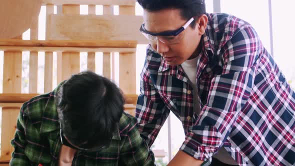 Carpenter Asian man teaching his son how to work with wood in workshop.