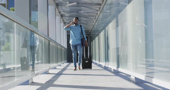 Video of african american man walking with suitcase and using smartphone