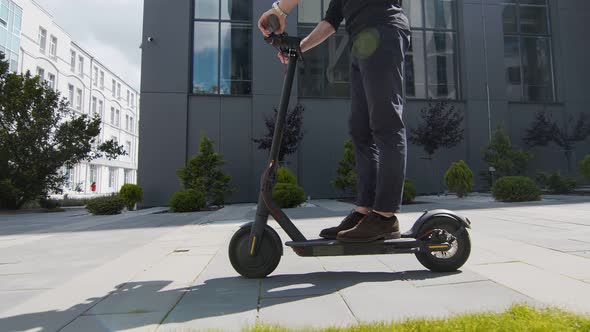 Legs of a Man Riding an Electric Ecological Scooter. A Man Stands on the Platform of an Electric