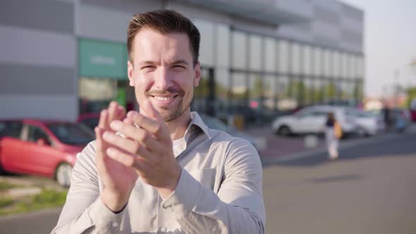 A Young Caucasian Man Applauds to the Camera and Nods with a Smile in an Urban Area