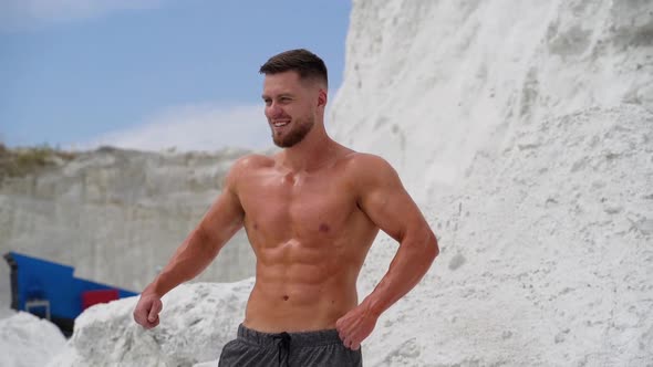 Bearded man with muscular body poses on white mountain background.