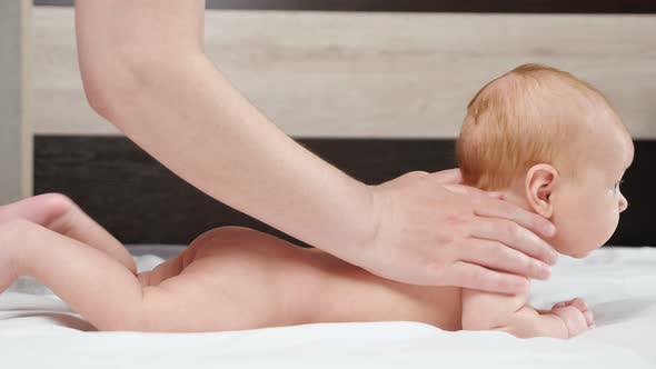 Mother Massages Back of Newborn Girl Lying on Bed at Home
