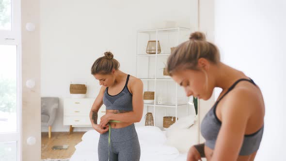 Sporty Girl Measures Waist with Measuring Tape Rejoicing By Weight Loss Looking at Mirror in White