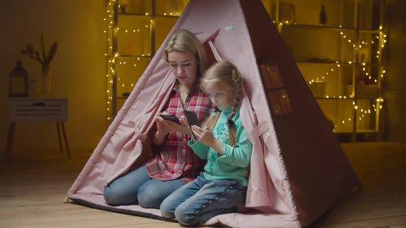 Busy with Phones Mom and Child Sitting in Kid Tent