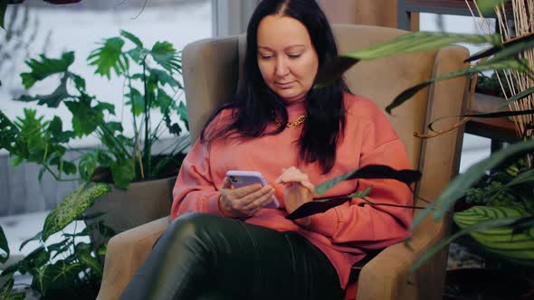 Woman Using Smartphone While Sitting Near Green Plants Indoors