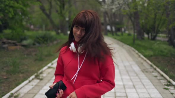 Woman with headphones and a phone in her hands, walks through the park, turning around and smilin