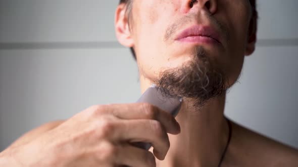 a young man cuts his beard and mustache with an electric razor