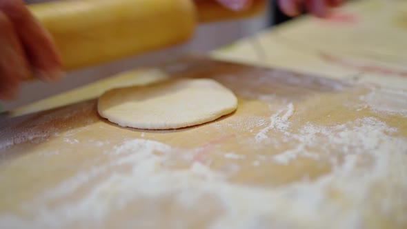 Female Hands Roll Out a Piece of Dough with a Rolling Pin