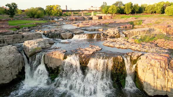 Drone view of Falls Park waterfall in Sioux Falls, South Dakota with sun gleaming off the water.