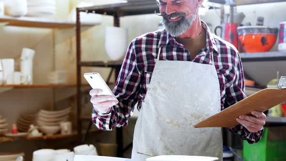 Male potter using mobile phone while writing in notepad 4k