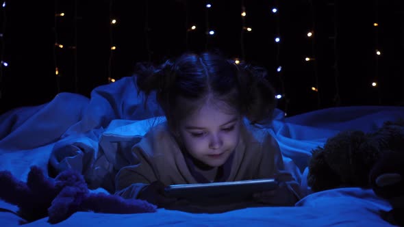 Child Is Lying on a Bed Holding a Laptop and Watching a Cartoon. Bokeh Background