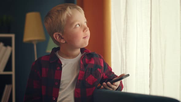 Little Cute Kid Boy Sitting on Sofa Using Smartphone at Home alt