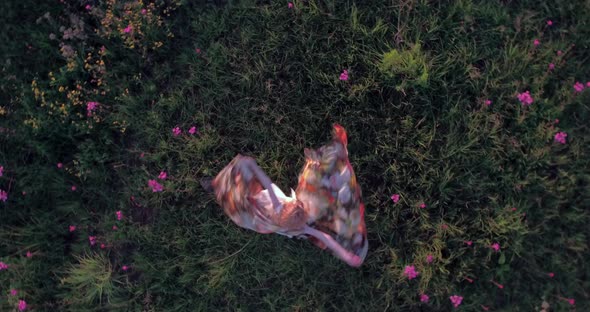 A bird's-eye, 4k drone footage, view of a beautiful young woman in a colorful dress twirling around