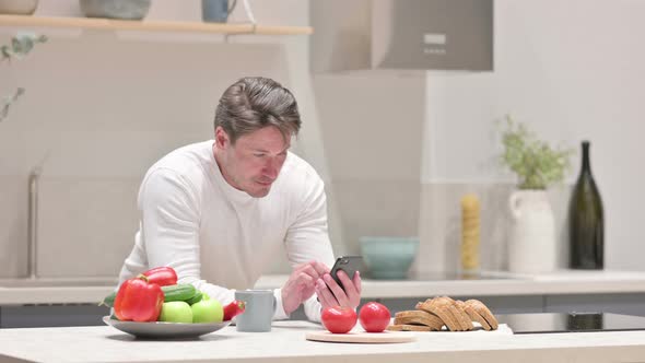 Middle Aged Man Using Smartphone While Standing in Kitchen