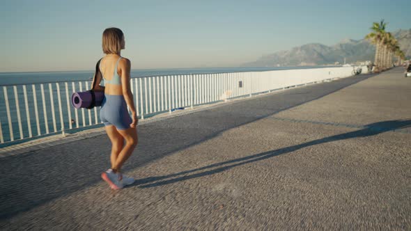 Sporty Young Athletic Girl with a Yoga Mat Walking Over a Bridge