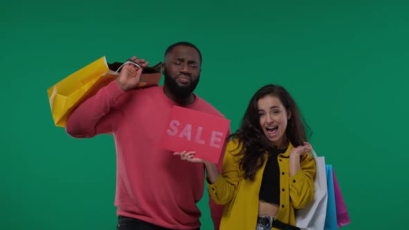 Attractive Young Couple Black Man and White Woman with Sale Sign and Shopping Bags on on Green