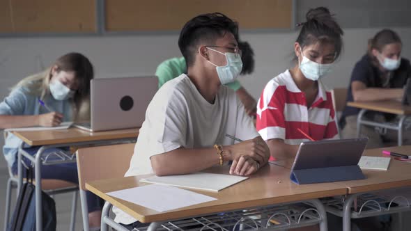 Multi Ethnic High School Students with Protective Face Mask Writing Notes and Using Laptops