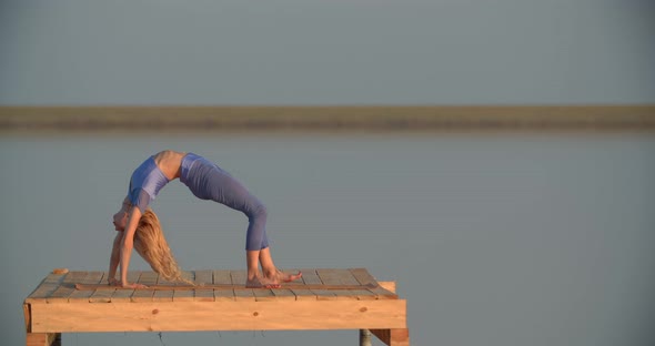 Woman in Blue Sportswear is Doing a Bridge Yoga Pose on a Wooden Platform