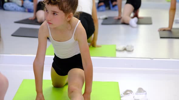 The child trains in the dance studio in the hall on the mat, does stretching exercises and abs, sits