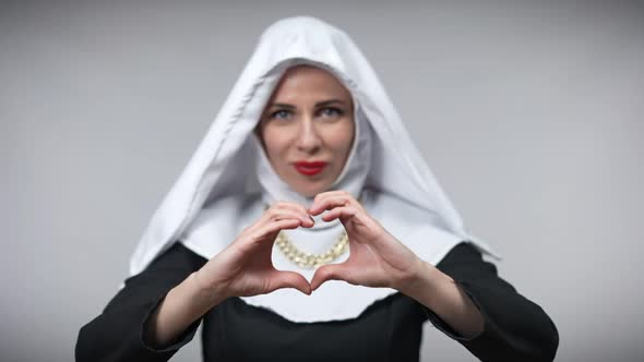 Closeup Female Hands Making Heart Shape with Blurred Caucasian Woman in Nun Costume Smiling Looking