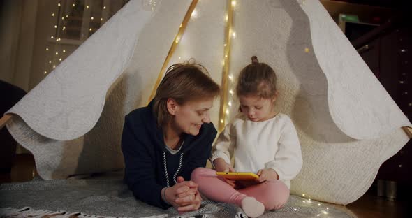 Happy Woman with Her Daughter at Smiling and Talking in Tent  Using Tablet