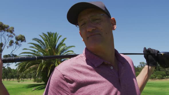 Portrait of caucasian senior man with golf club smiling at golf course on a bright sunny day