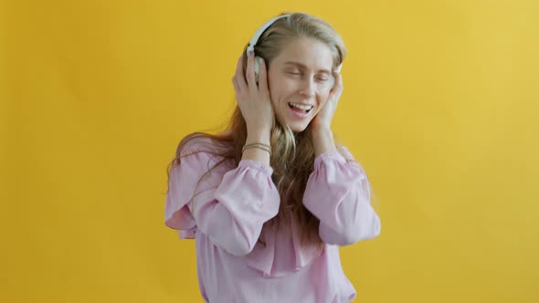 Portrait of Happy Girl Listening to Music Through Headphones and Singing on Yellow Background