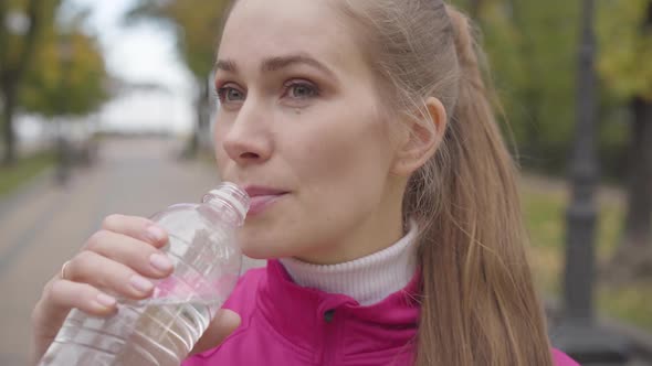 Close-up Face of a Tired Caucasian Sportswoman with Grey Eyes Drinking Water and Wiping Her Forehead