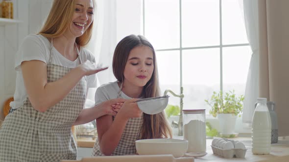Adult Mother with Long Hair Teaches to Cook Little Daughter Teenager Sifting Flour Together Through