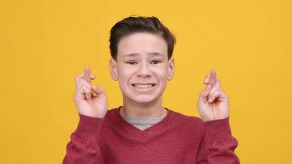 Boy Keeping Fingers Crossed For Good Luck Over Yellow Background