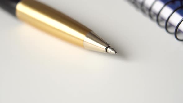 Golden black pen and closed notepad on white office desk. 