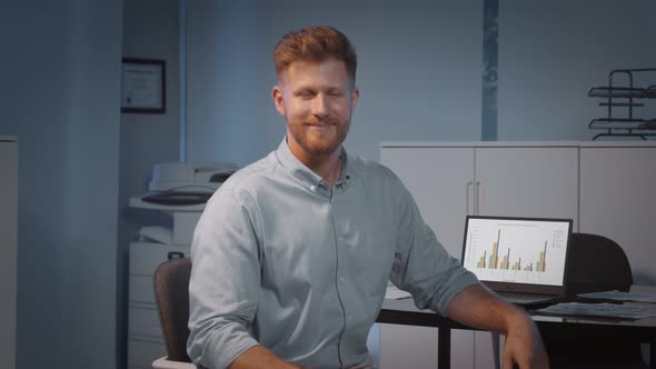 Young Businessman Sitting Relaxed Behind Office Desk Smiling at Camera