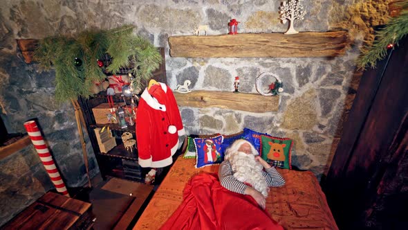 Santa Claus is sleeping in specially decorated room in his bed.