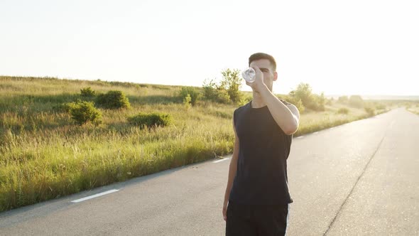 Confident Jogger Walking on the Road at Nature with Sunset and Drinking Water