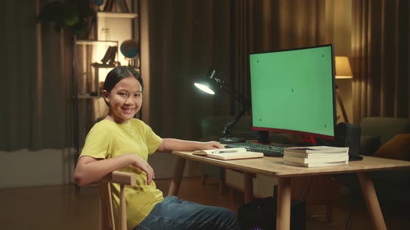 Girl Learning Online With Mock Up Computer Green Screen From Home, She Turns And Warmly Smiles